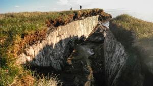 People standing on a cliff where a large block of frozen ground has broken off