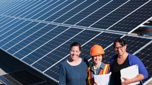 Three women standing in front of an installed solar grid