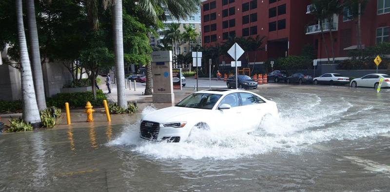 Car driving through water on street in a downtown scene