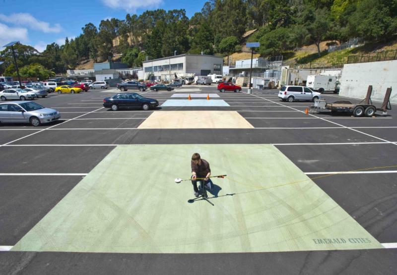 Person kneeling in a light-green square of pavement, with other colors in the background